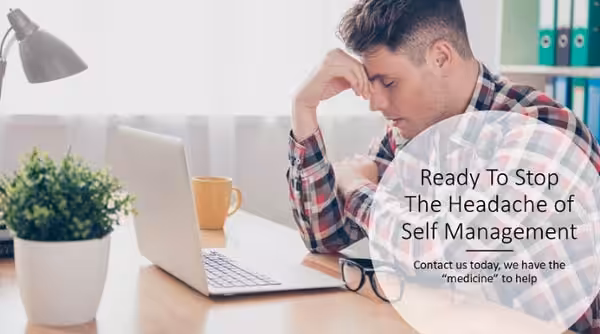 Stop the Headache of Self Property Management. Contact Management One Property Management Grimacing man sitting at a table in front of his laptop
