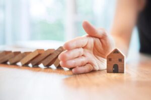 Hands protecting house model from wooden blocks